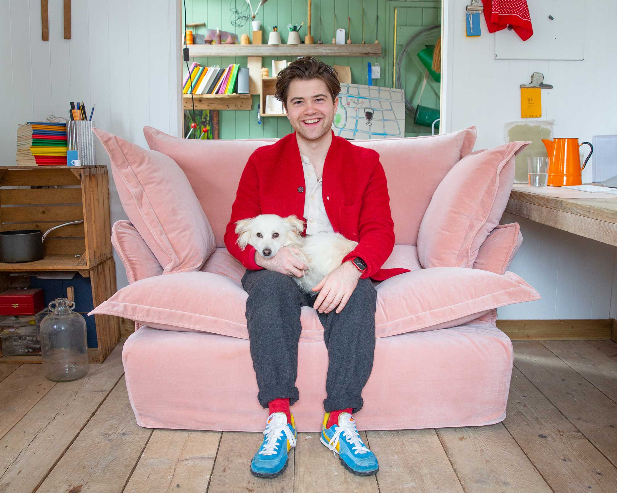 Felix Conran and Apollo the dog on a Maker&Son plaster pink velvet loveseat in Song pillow edge in his studio.