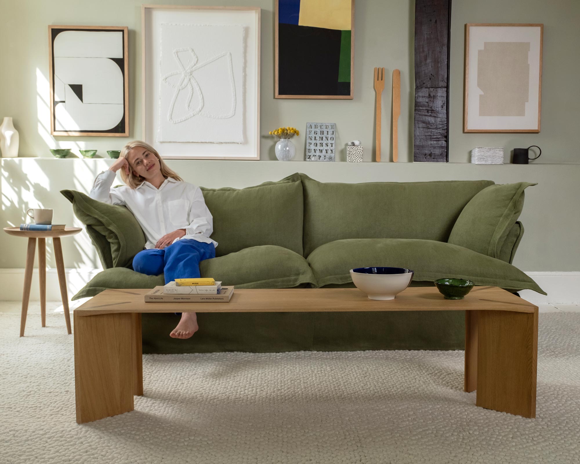 Marnie sitting on the left hand side of a malachite green sofa. In front of her is a Dove coffee table styled with a large bowl and books.