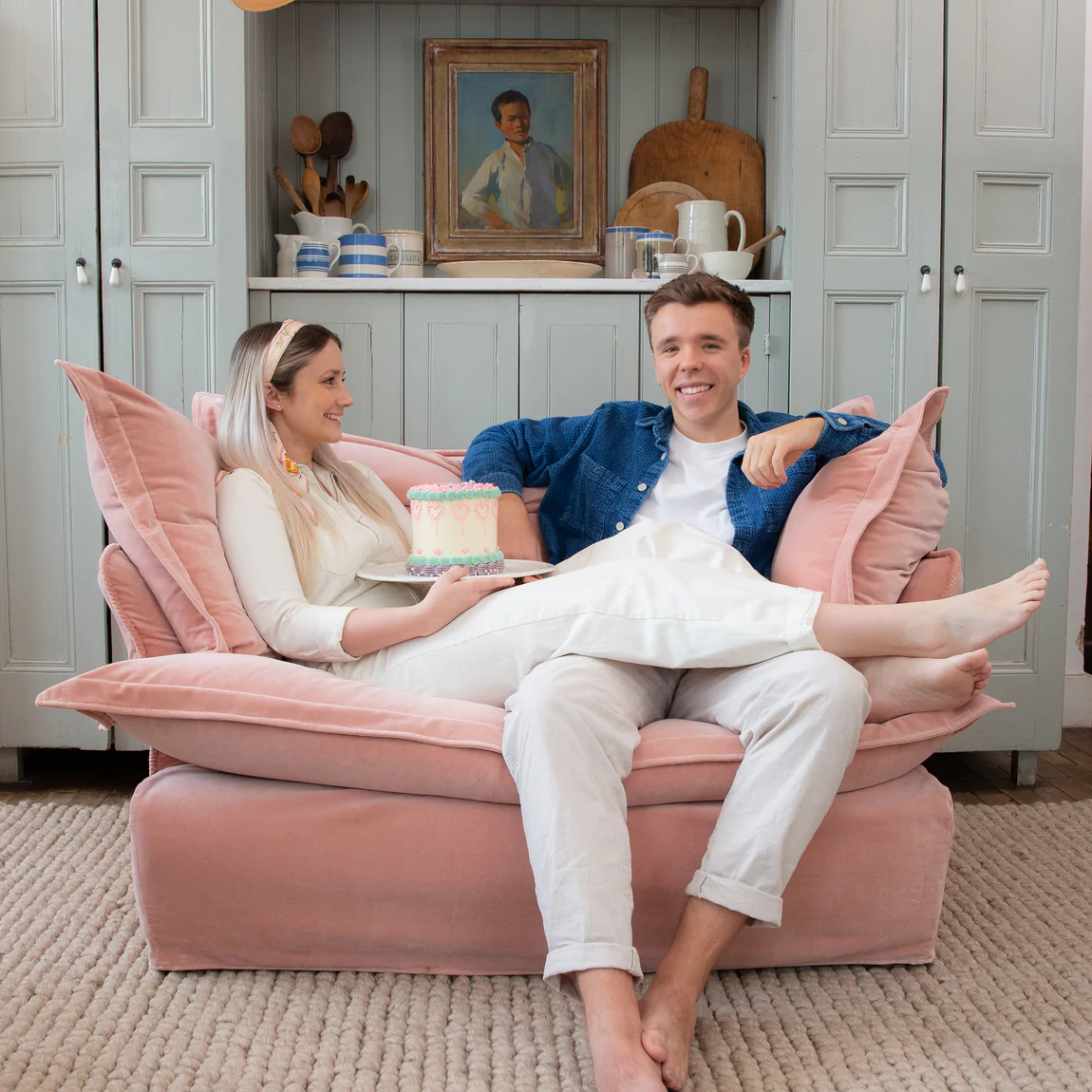 Couple sitting happily on a Maker and son plaster pink velvet loveseat in Song pillow edge.