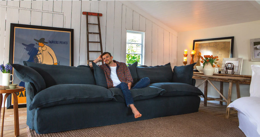 Freddie sitting in the middle of a Large Song pillow edge Sofa in Hawk's Eye blue 100% Italian linen.